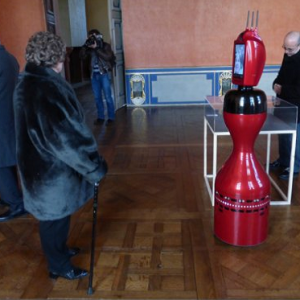 Robot Norio dans une salle d’un bâtiment ancien, face à des visiteurs.