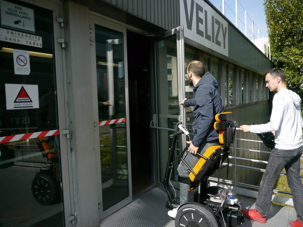 Diapo 3 : Personne se déplaçant  dans un fauteuil Gyrolift en position debout entrant dans un bâtiment.