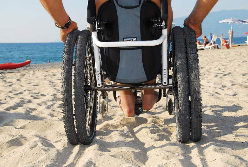 Diapo 1 : Fauteuil roulant à roues larges, roulant sur du sable.