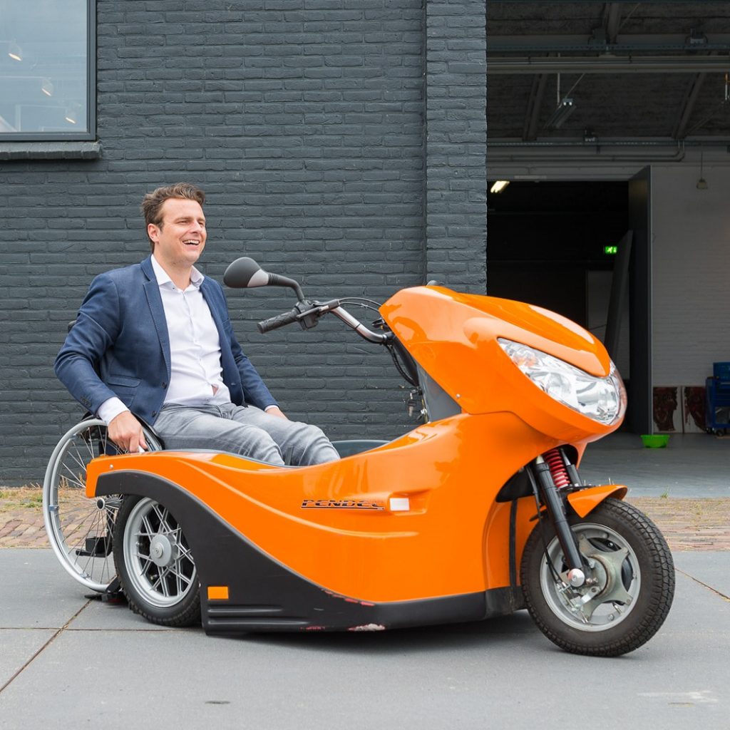 Diapo 5 : Personne en fauteuil roulant, s'arrimant à un Pendel Mobility Scooter.