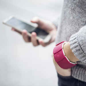 Personne portant un bracelet Unitact au poignet gauche, et utilisant un smartphone de la main droite.