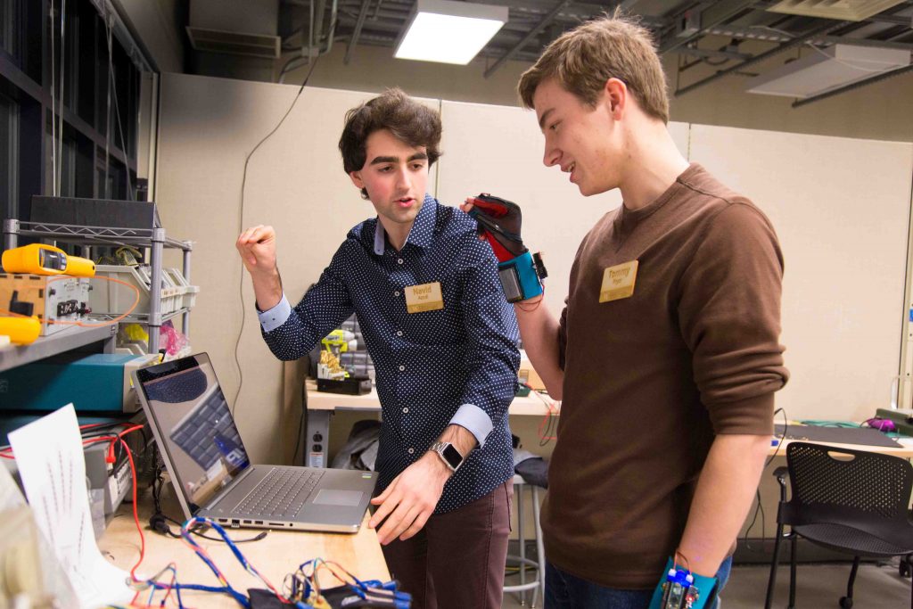 Diapo 2 : Deux personnes testant des prototypes de gants Sign Aloud dans un espace de travail.