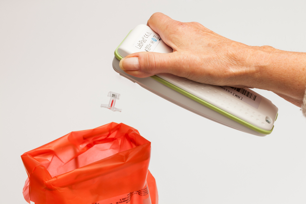 Diapo 5 : Personne éjectant une languette plastique de test sanguin usagée de son appareil LabPad.