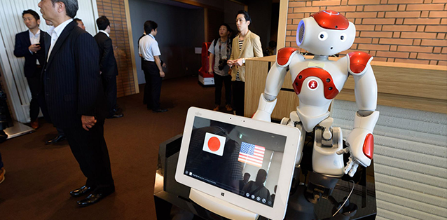 Diapo 2 : Robot Nao, sur une table à coté d'un ordinateur affichant les drapeau Américains et Japonais.