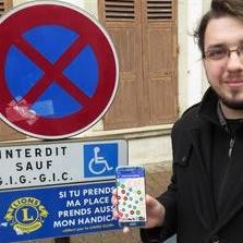 Homme devant une place réservée aux personnes handicapées montrant l’application Stationnement Handicapé sur son téléphone