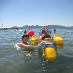 Image de deux filles à la plage dont une handicapée qui est sur un flotteur dans l’eau