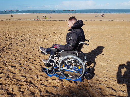 Diapo 6 : photo représentant une personne sur un fauteuil roulant sur du sable