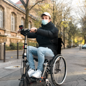 Photo d’une personne en fauteuil roulant accroché à une trottinette par le dispositif globe trotter