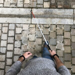 Homme qui marche avec une canne blanche dans la main, et qui a aux poignets les bracelets N-Vibe