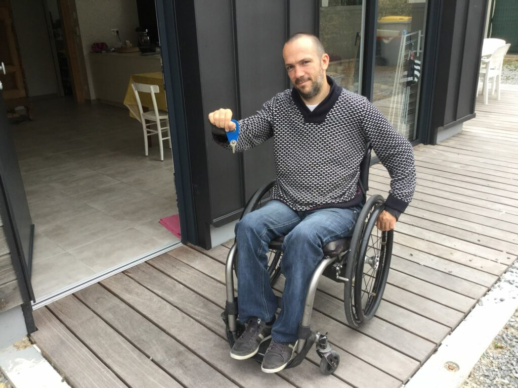 Diapo 3 : Photo d'un homme en fauteuil roulant avec des clés dans la main devant une maison