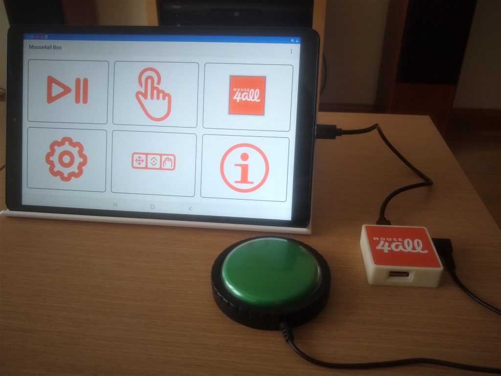 Diapo 2 : Une tablette avec l'application Mouse4All, un contacteur vert connecté au boitier sur une table en bois