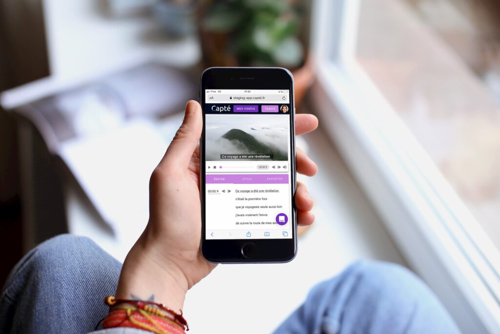 Diapo 2 : Main d'une personne tenant un téléphone avec une vidéo sous-titrée par Capté dessus