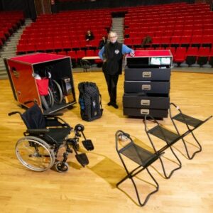 Photo d’une personne dans un théâtre avec une Handibox contenant des sièges cannes, des fauteuils roulants et d’autres matériels