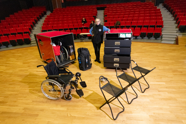 Diapo 2 : Photo d'une personne dans un théâtre avec une Handibox contenant des sièges cannes, des fauteuils roulants et d'autres matériels